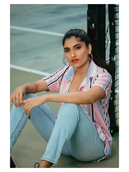 A casual and stylish outdoor portrait. The model is seated on a tennis court, giving the shot a relaxed, athletic vibe.