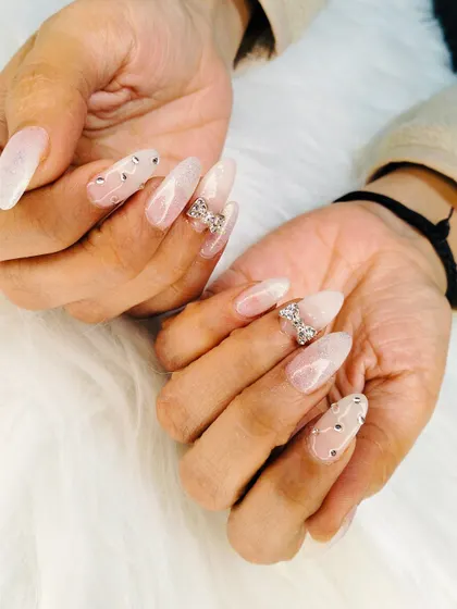 An angelic set of long, almond-shaped extensions with a milky white base, adorned with sparkling rhinestone bows and scattered gems.