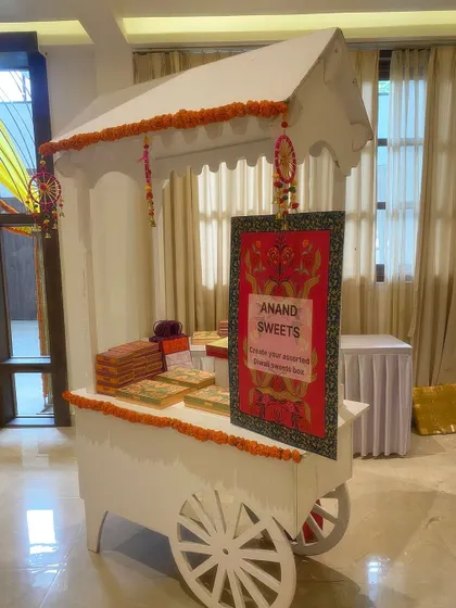 A traditional sweets cart from Anand Sweets, set up for a Diwali celebration. The cart is decorated with marigold garlands, adding an authentic and festive touch to the party.