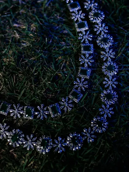 An artistic, low-light shot of a diamond and emerald necklace on the grass.