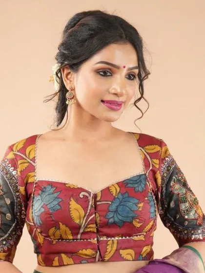 This sweetheart neck blouse features a lovely floral Kalamkari design. The sleeves have a contrasting black panel with intricate motifs, adding depth to the design.