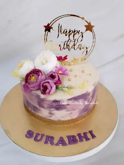 A beautiful no-fondant birthday cake with a purple watercolor effect. The cake is decorated with a small floral arrangement and a custom gold topper for an artistic touch.