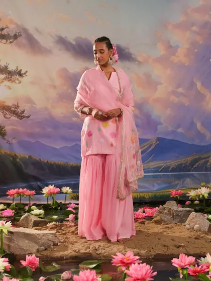 A full-length shot of a pink sharara set from the Gulnaar collection, set against a dreamy, painted backdrop.