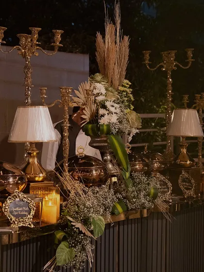 A close-up of a lush and layered buffet tablescape. We combine dried pampas grass, fresh flowers, classic table lamps, and candelabras to create a rich, textured look.