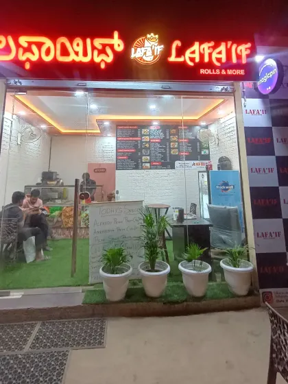 Here's a look at my cozy eatery at night. I've created a clean and bright space for you to enjoy all your favorite vegetarian snacks, from Vada Pav to Chole Bhature. I'm located right near the Bhartiya city back gate, making it an easy stop for your evening cravings.