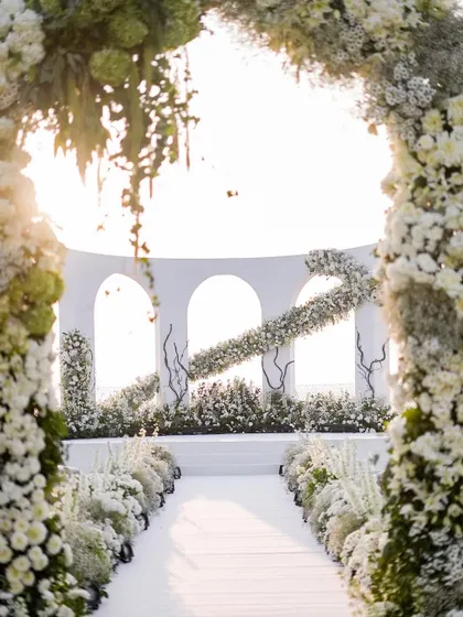 A closer look at the wedding mandap, framed by a lush floral arch. The design creates a beautiful window to the ceremony, with the setting sun adding a warm, golden glow.