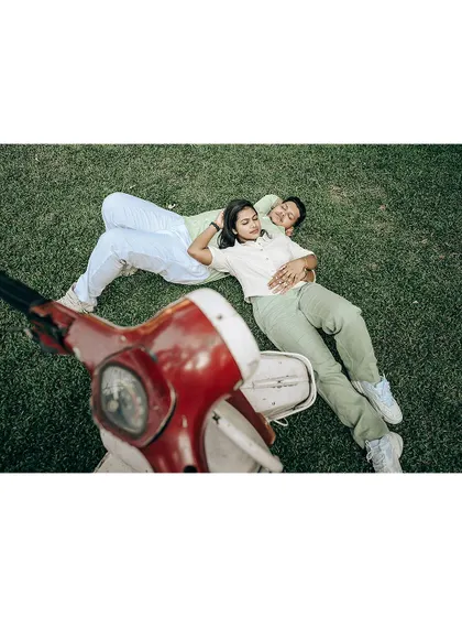 A creative aerial shot of a couple relaxing on the grass, with a vintage scooter in the foreground.