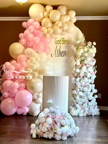 A lovely pastel balloon and floral decoration for a baptism. The arrangement in shades of pink and cream frames a custom "God Bless" backdrop, creating a soft and celebratory atmosphere.