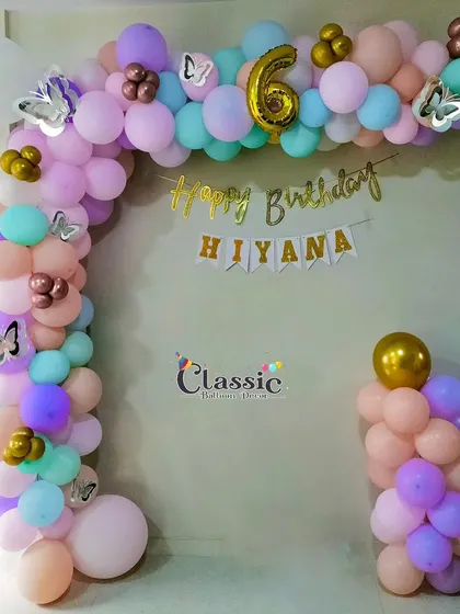 A pastel-colored balloon arch with butterfly accents for a 6th birthday, creating a sweet and simple decoration for a home party.