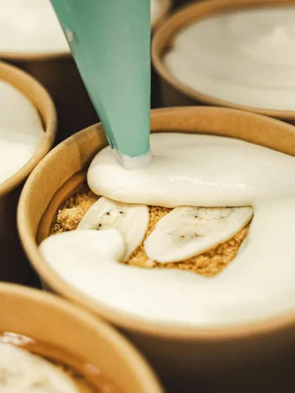 A generous layer of sweet cream is piped over the bananas and biscuit crumble.