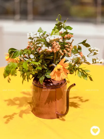 A rustic watering can used as a vase for a floral centerpiece, adding a unique and charming touch to the table decor.