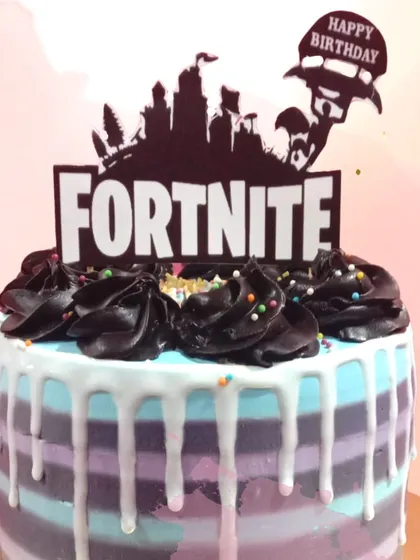 A victory royale for a Fortnite fan's birthday. This cake captures the game's aesthetic with its purple and blue stripes, white chocolate drip, and iconic logo topper, making it the perfect fuel for a gaming party.