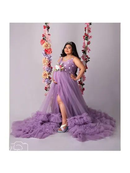 The full view of this gorgeous mama-to-be on the floral swing, showcasing the incredible length and texture of the purple ruffled gown.