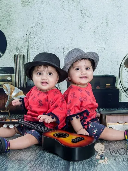 Twin musicians! These two babies are sitting with a guitar in a retro-themed studio with a record player and old-fashioned fan. It's a super cute and creative concept for a twin photoshoot.