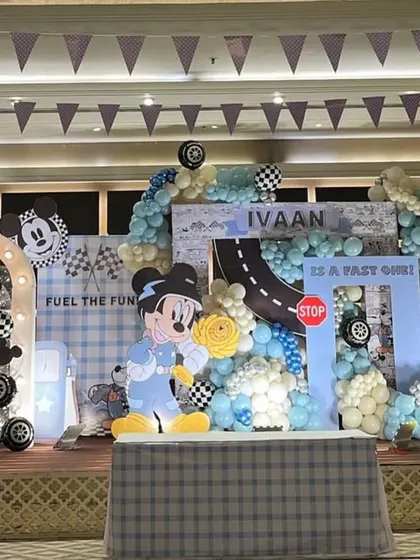 A full view of the Mickey the Racer stage. The setup includes a gas station prop and checkered flag banners, creating a complete racetrack environment for Ivaan's 'Fast One' birthday.