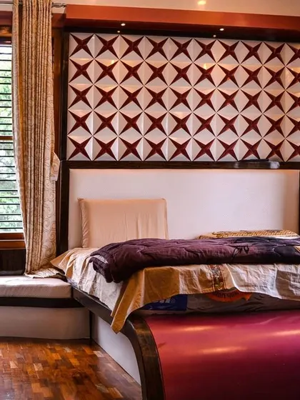 This bedroom showcases a bold, custom 3D accent wall behind the bed, with a geometric star pattern in red and white. The room also features warm wooden flooring and a built-in window seat for a cozy reading nook.