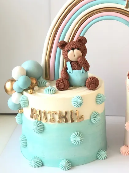 A close-up of a "twin cake" set, this one for a baby boy with a cute teddy bear and a blue and gold color scheme.