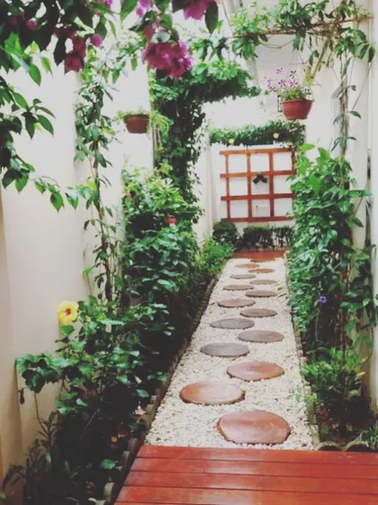 A beautiful green pathway created in a side yard. We used a combination of climbers on the walls, hanging baskets, and a gravel path with wooden stepping stones to make this narrow space feel like a secret garden.