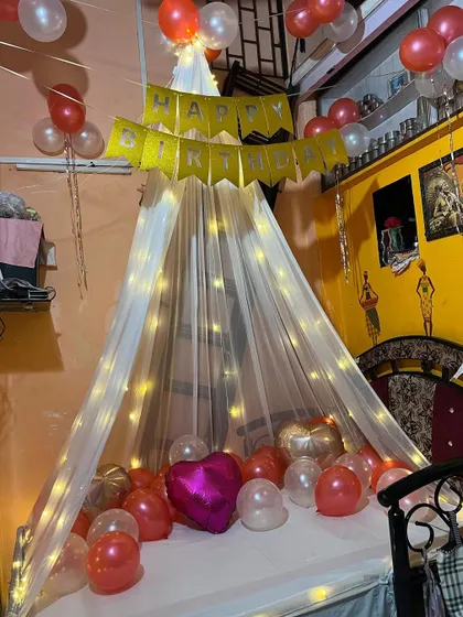 A wider view of the birthday canopy setup, showing how the balloons and lights transform a simple room into a special space for celebration. The combination of the banner, canopy, and balloons makes for a complete package.