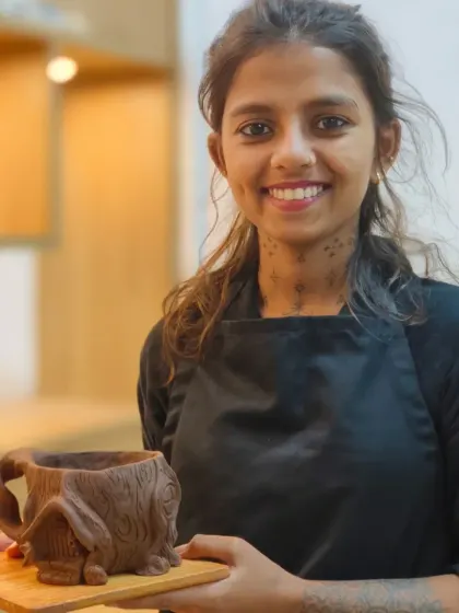 A student proudly displays her finished house-shaped mug, complete with intricate details like a textured roof and a twisted handle. Hand-building allows for endless creativity and personalization.