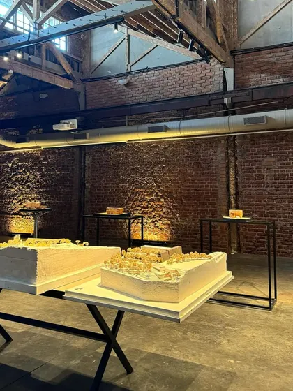 The exhibition space at IF.BE, featuring physical models of our projects. The raw brick walls and concrete floor of the restored ice factory provide a powerful backdrop for the refined architectural models.