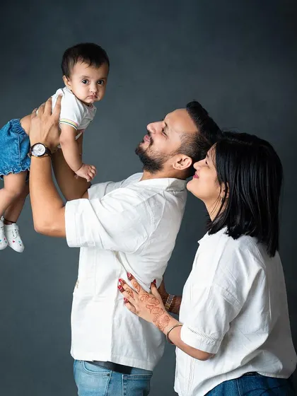 A candid and joyful family moment, with mom and dad lifting their laughing baby.