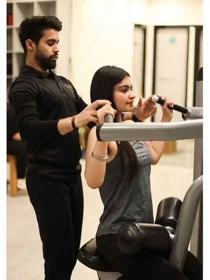 With a trainer's guidance, this client works on her back and shoulder strength using a pull-down machine, ensuring each repetition counts.