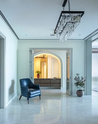 This elegant hallway in 'The 18th' project in Gurgaon uses classic paneling and a striking chandelier to create a grand entrance. The design balances traditional elements with modern touches, like the bold green armchair that adds a pop of color.