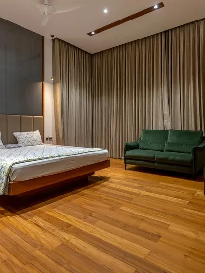 A spacious and moody bedroom with dark wood flooring, a fabric-paneled headboard, and full blackout curtains, designed for ultimate comfort and relaxation.
