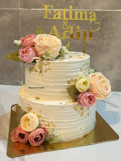Another view of this romantic two-tier engagement cake, highlighting the placement of the fresh pastel flowers and the elegant custom name topper.
