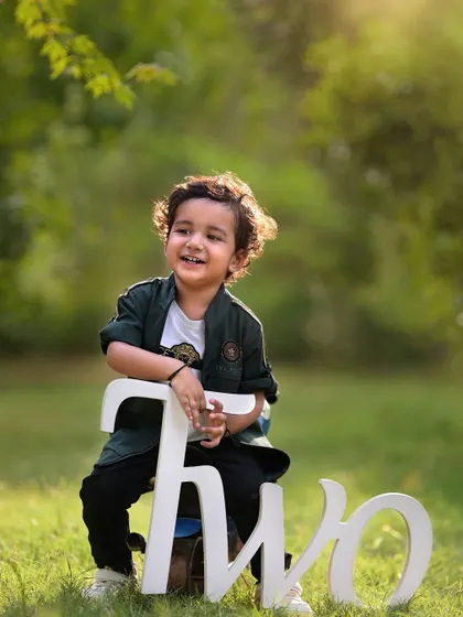 Celebrating the big TWO. This outdoor milestone portrait captures the pride and joy of a two-year-old, with beautiful natural light and a simple prop to mark the occasion.