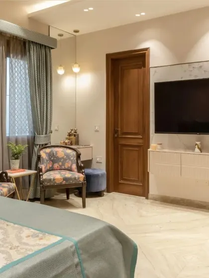 The room includes a cozy sitting area with floral print chairs and a sleek TV unit, creating a perfect balance of relaxation and entertainment.