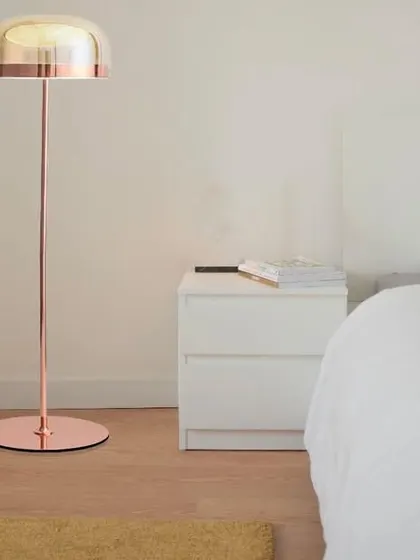 This dainty metal floor lamp features a sleek copper finish and a glass dome shade. Its minimalist design is perfect for a modern bedroom or living space, providing soft, ambient light without taking up much space.