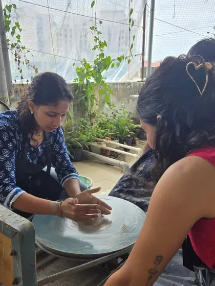 A participant learns the basics of wheel throwing, her hands gently guiding the clay. The lush green plants in the background highlight our open, airy studio space.