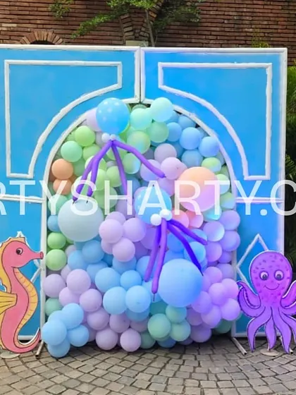 A cute photo booth with a blue arched backdrop and various sea creature cutouts like a seahorse, octopus, and crab.