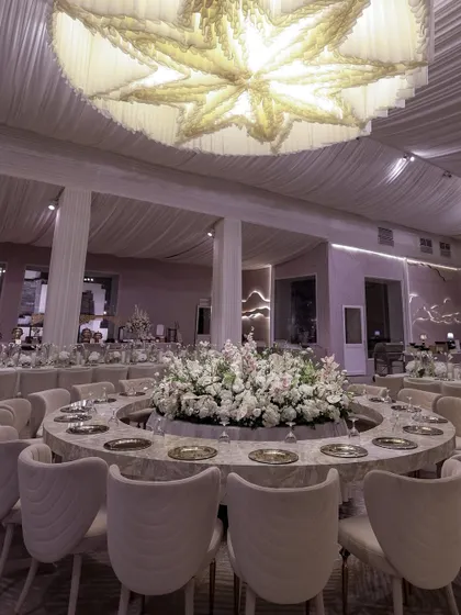 A circular dining table with a massive floral centerpiece, set under a grand, custom-made chandelier, exuding pure elegance.