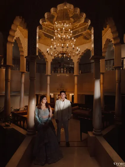 A dramatic, low-light portrait of a couple under a grand chandelier in a palace, creating a moody and opulent atmosphere.