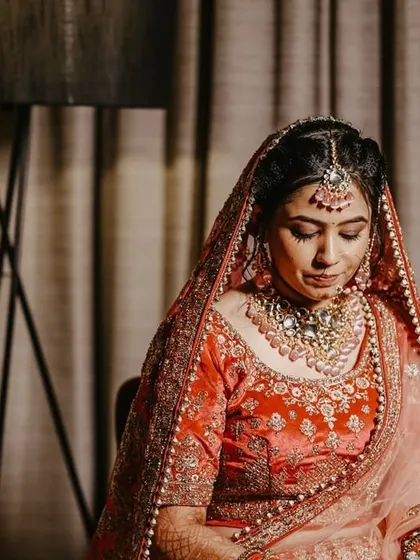 A pensive portrait of the bride, seated and looking down, showcasing the intricate details of her lehenga and jewelry.