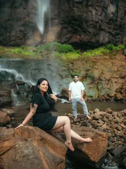 A creative portrait with the bride in the foreground and the groom in the back, set against a waterfall.