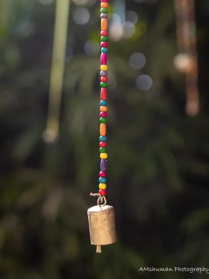 A close-up of a handcrafted bell on a colorful beaded string, part of an interactive installation that invited children to make music and play.