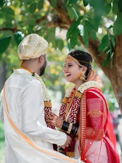 A candid moment of pure laughter between the bride and groom, captured under a canopy of trees.