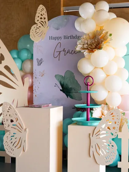 A detailed shot of the butterfly theme, focusing on the personalized "Happy Birthday Grace" backdrop. The combination of teal and cream balloons with delicate flower accents adds a touch of elegance.