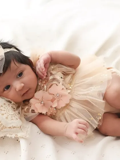 A precious moment of stillness with eyes wide open. This little one, dressed in a beautiful peach-colored outfit, looks curiously at the world from the comfort of a soft pillow.