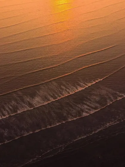 A close-up aerial shot of golden waves at sunset, highlighting the beautiful lines and textures of the water.