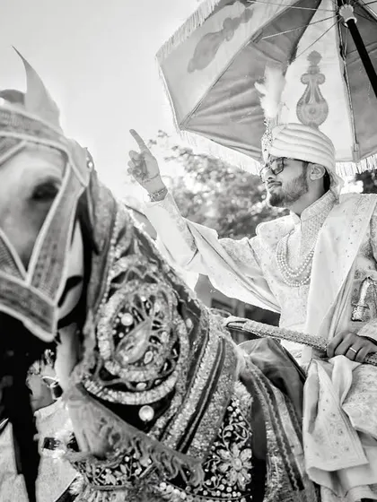 A dynamic black and white shot of the groom's baraat. The low angle and focus on the groom on his horse capture the energy and tradition of the procession.