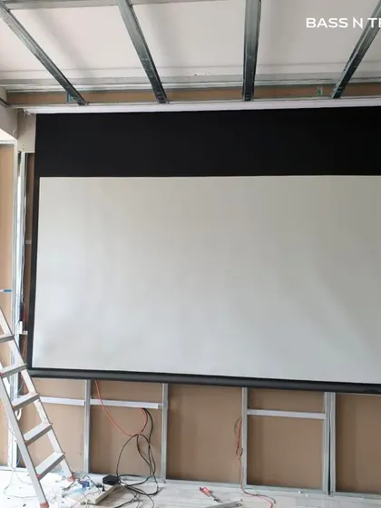A big screen experience doesn't have to mean a permanent black rectangle on your wall. This image shows the installation of a retractable 4K projector screen, which disappears into the ceiling when not in use, offering a cinematic experience without compromising the room's design.