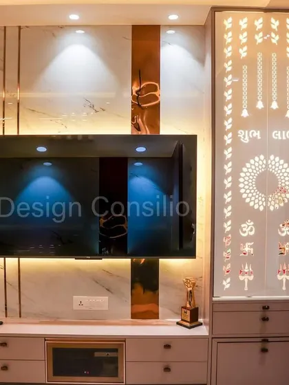 A beautiful living room where the TV unit and a compact pooja mandir share a wall. The CNC-cut jaali panel on the mandir is backlit, creating a divine glow that complements the modern entertainment setup.