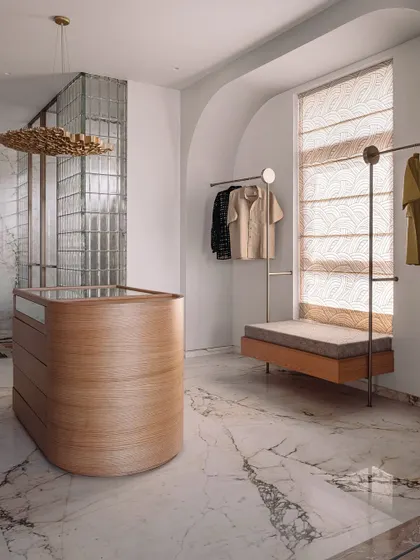 The walk-in closet features a curved wooden island dresser, minimalist clothing racks, and a beautiful veined marble floor.