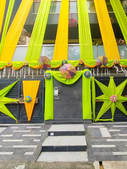 A fresh and vibrant theme using lime green and yellow drapes for a house front, perfect for a daytime summer wedding function.