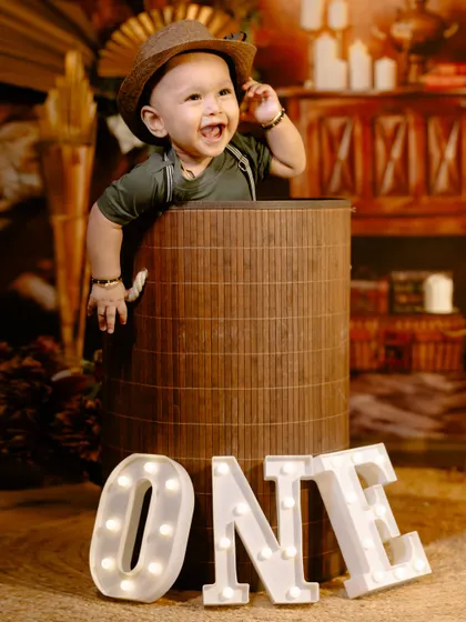 A big smile for a big milestone. This little boy celebrates turning one with light-up "ONE" letters and a rustic, warm-toned studio setup.